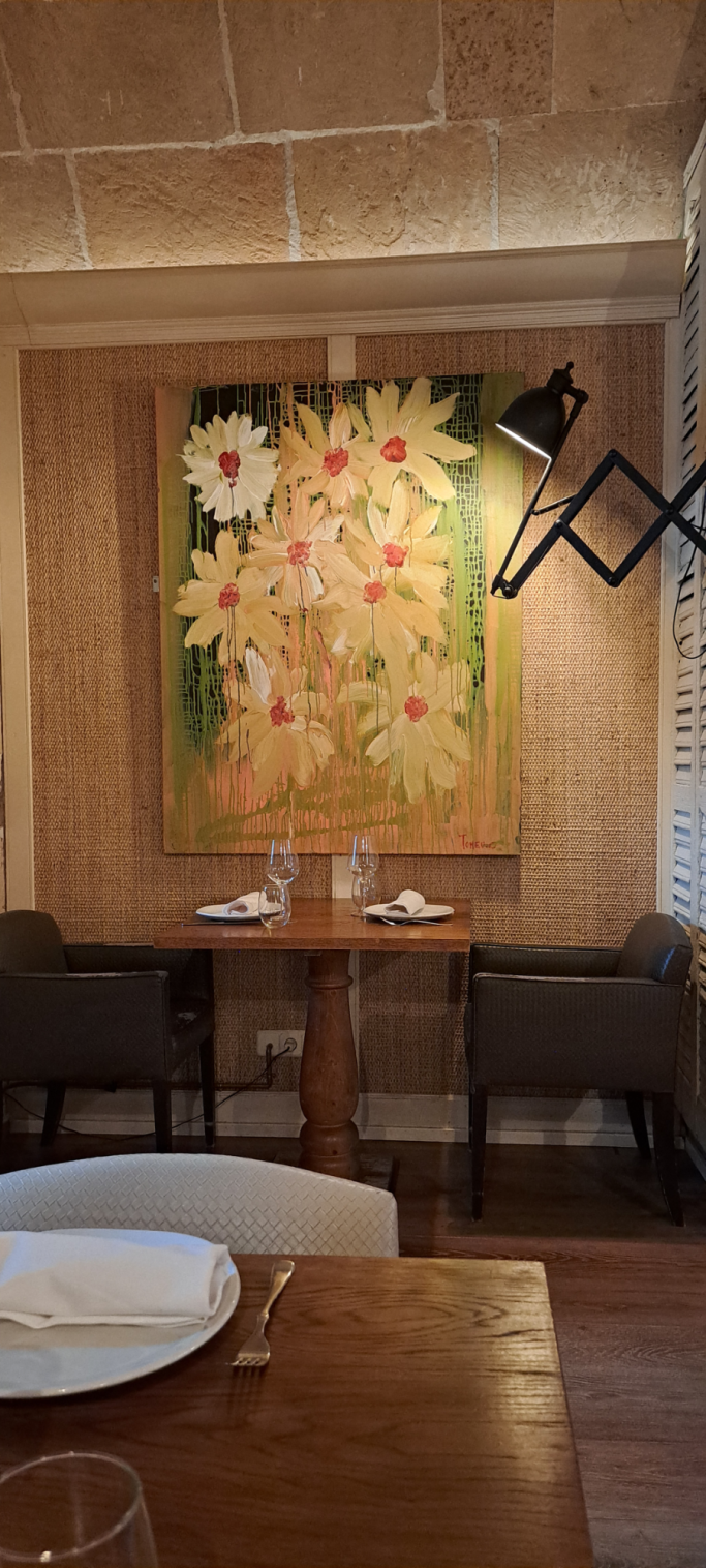 Mesa en el "Tast Club" con un cuadro de flores coloridas tipo Margaritas del pintor mallorquín Tomeu Cerda