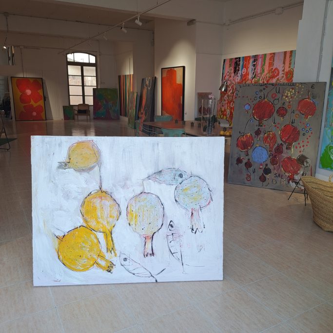 Lienzo con granadas amarillas y un pez en un estudio de arte. Fondo con obras diversas.