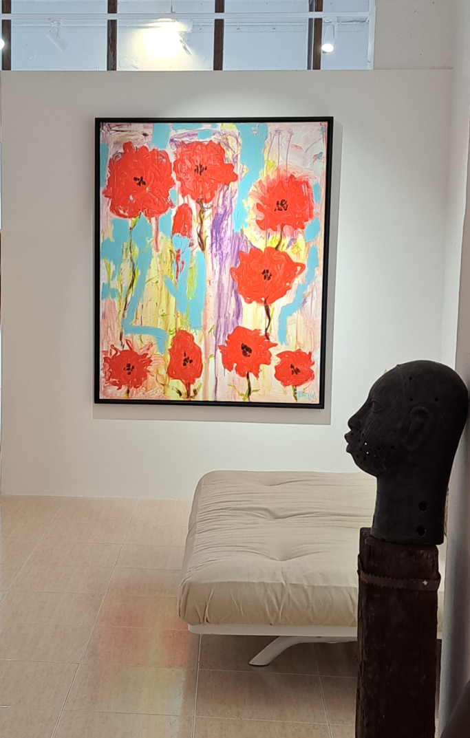 Cuadro con grandes flores rojas en un fondo colorido, junto a una escultura y un sofá.