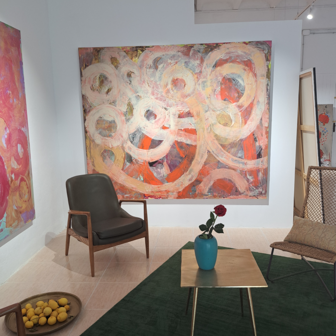 Sala con pintura abstracta en la pared, sillón, mesa y una rosa en un jarrón.