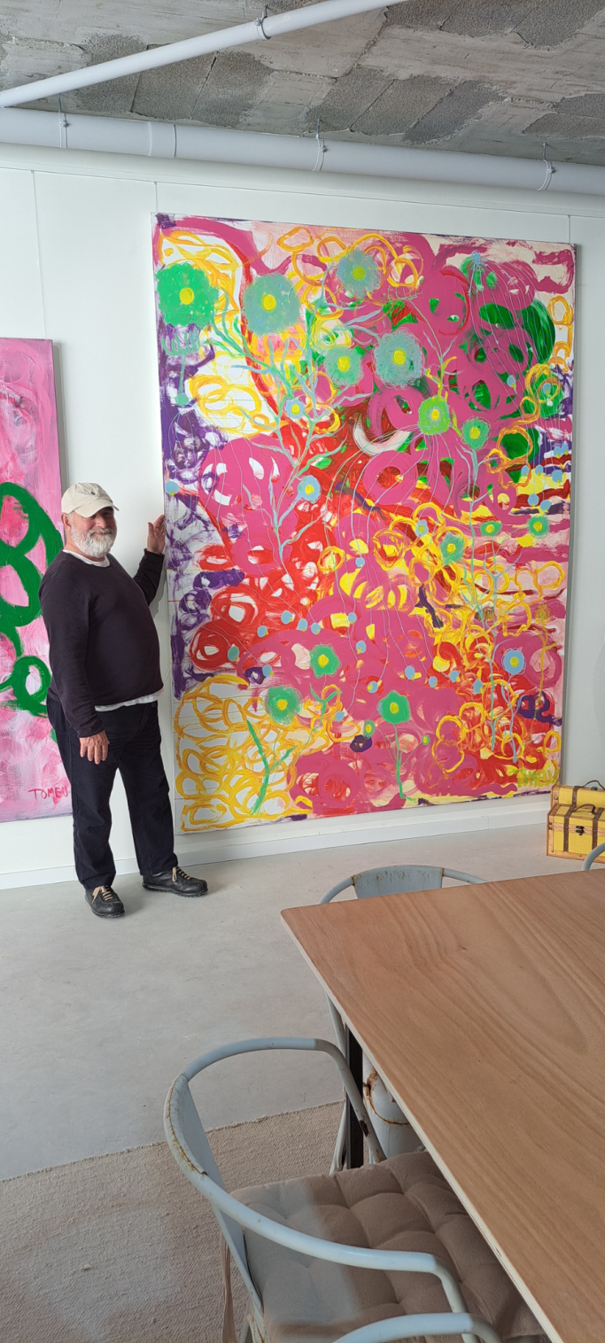 Persona de pie junto a un gran mural abstracto de colores vibrantes.