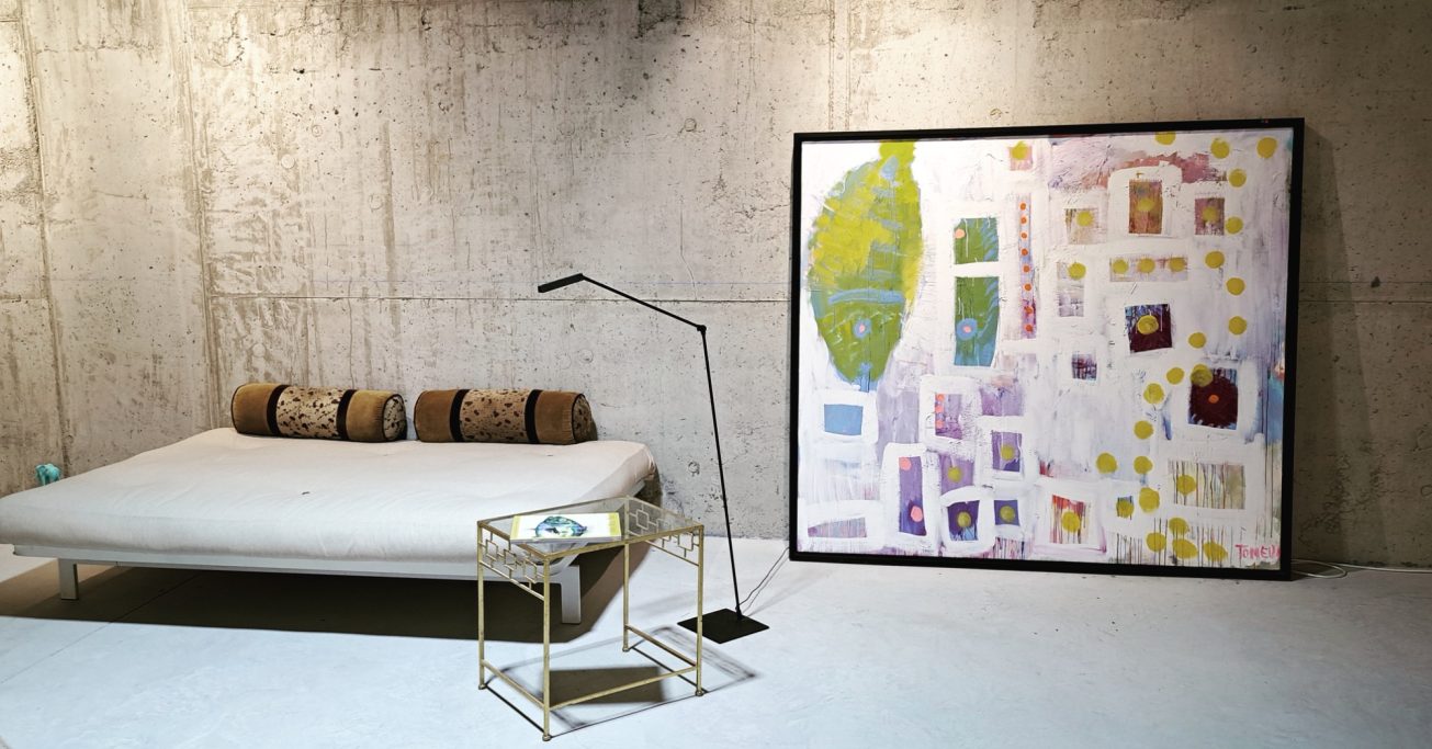 Sala moderna con sofá, lámpara y un mural colorido de mapas y figuras en la pared.