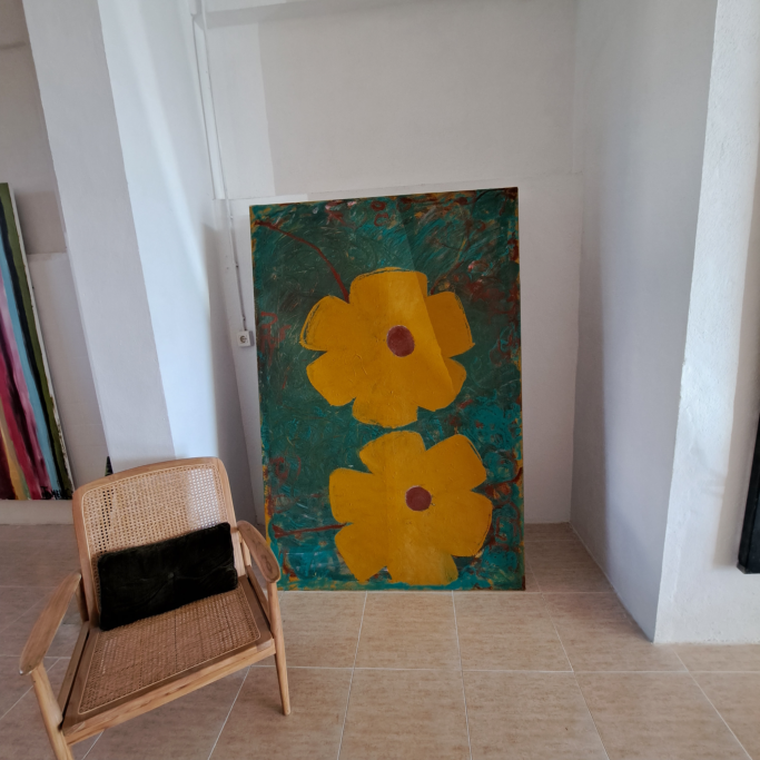Cuadro con dos flores amarillas sobre fondo verde, junto a una silla de madera.