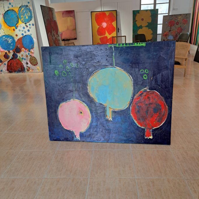 Pintura abstracta con tres granadas de colores sobre un fondo oscuro en una galería de arte.